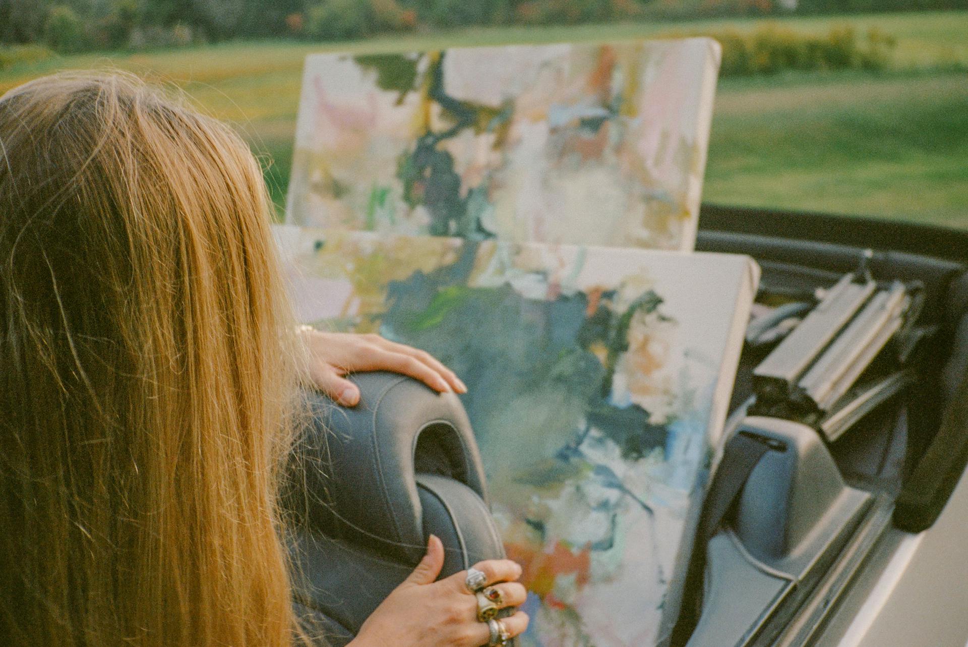 A woman looks at art that's in the backseat of a car