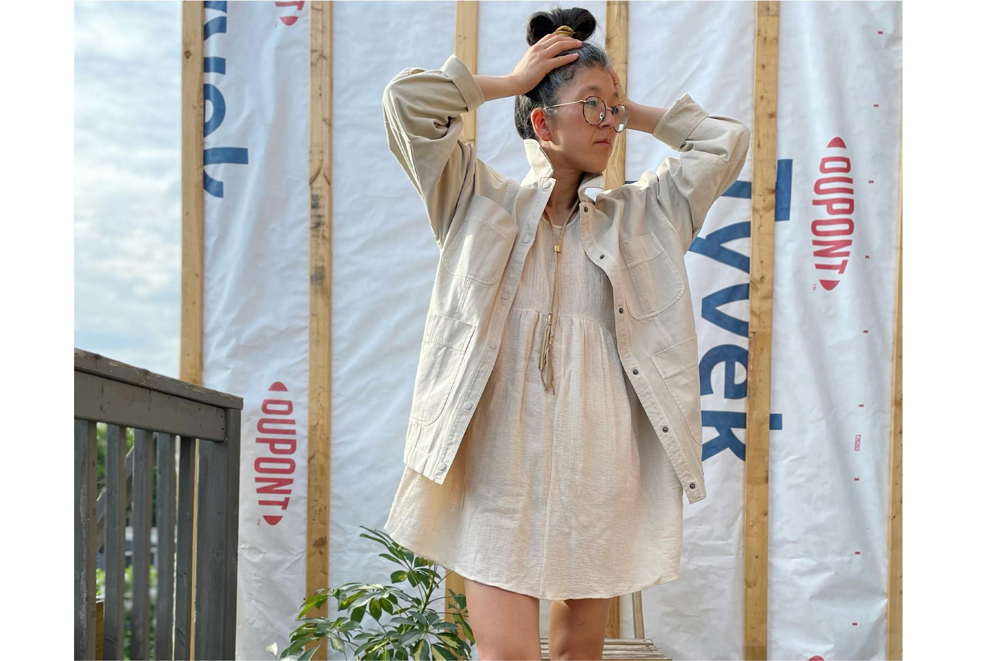 Erica Kim wears a light colored dress and stands outside, holding her hair.