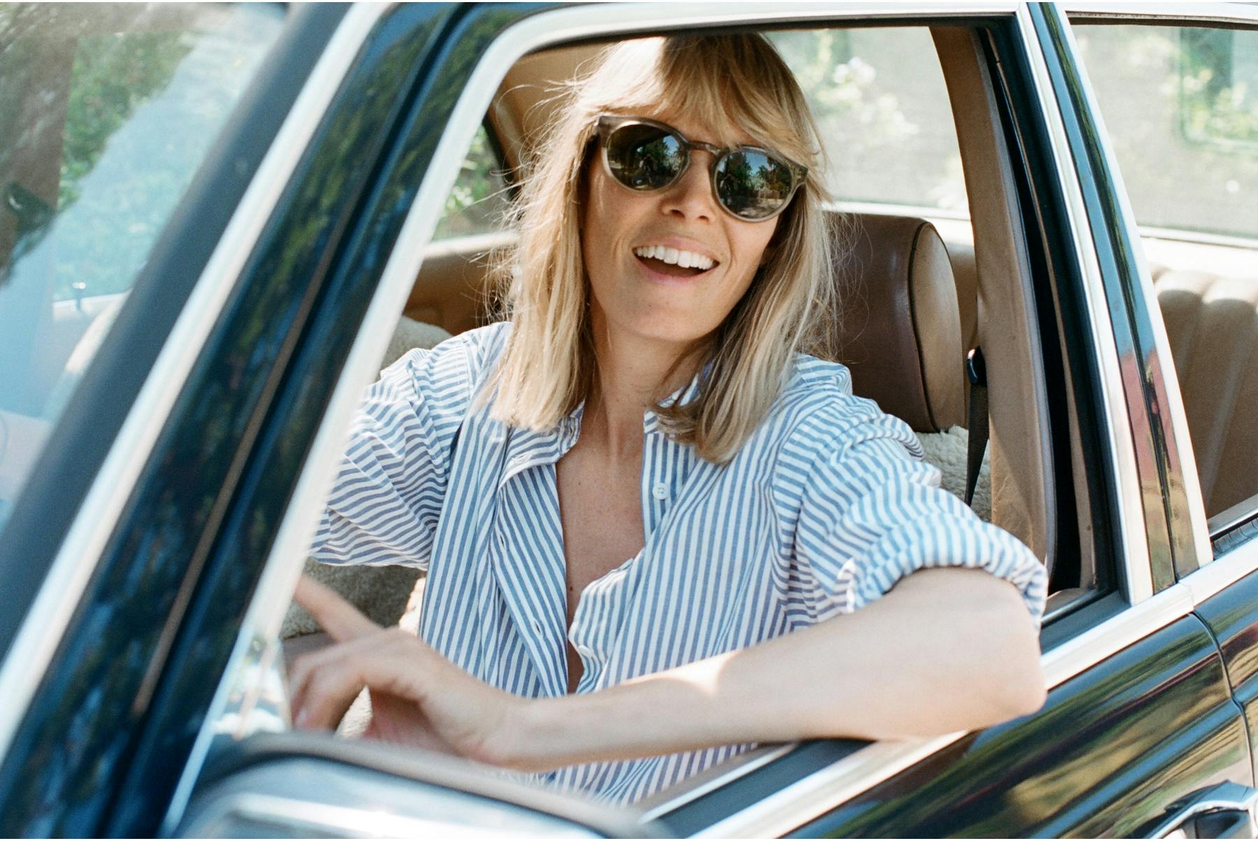 Jesse Kamm wears a light blouse and sunglasses while sitting in a car