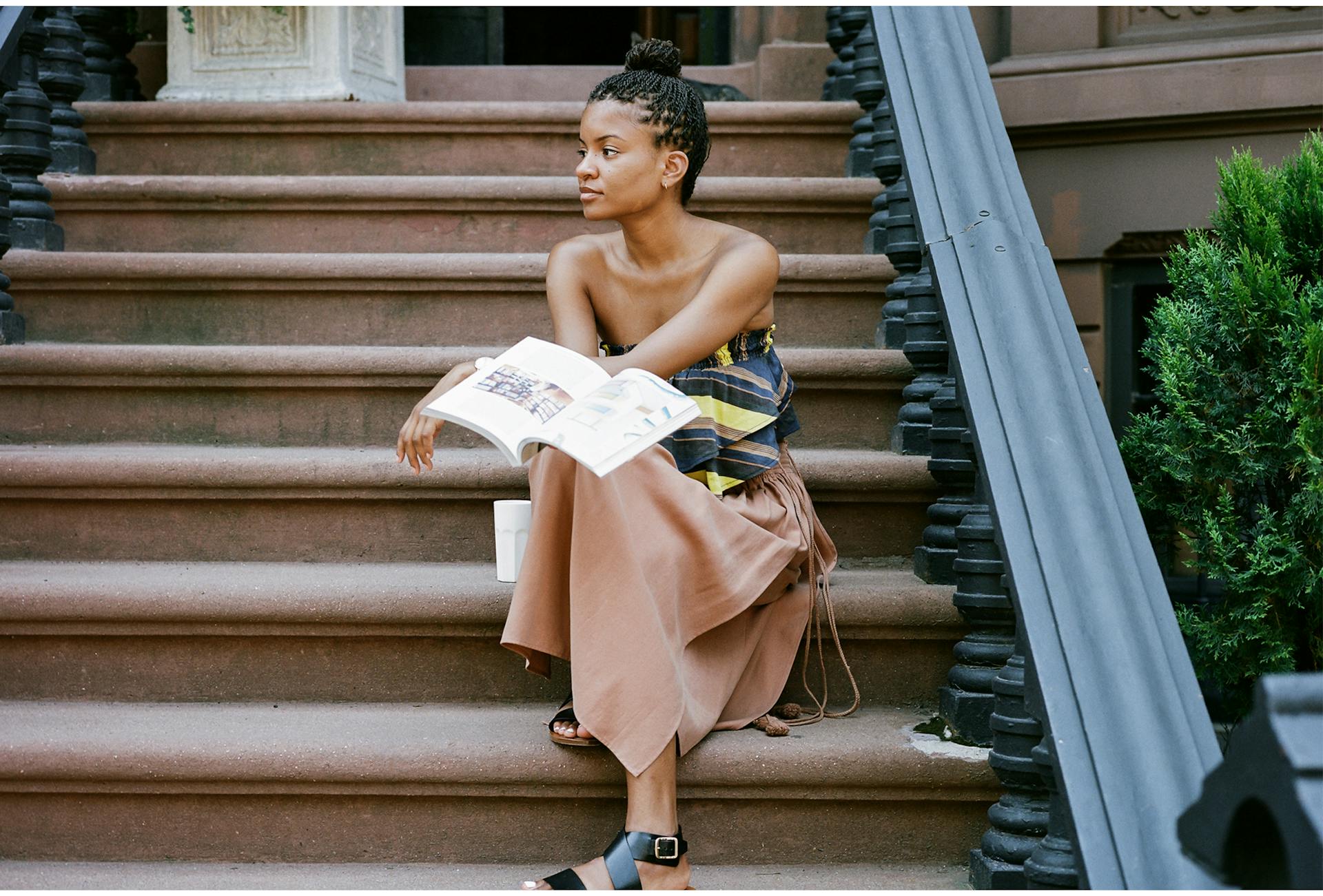 Kai Avent-deLeon sits on brownstone stoop while wearing a beige dress